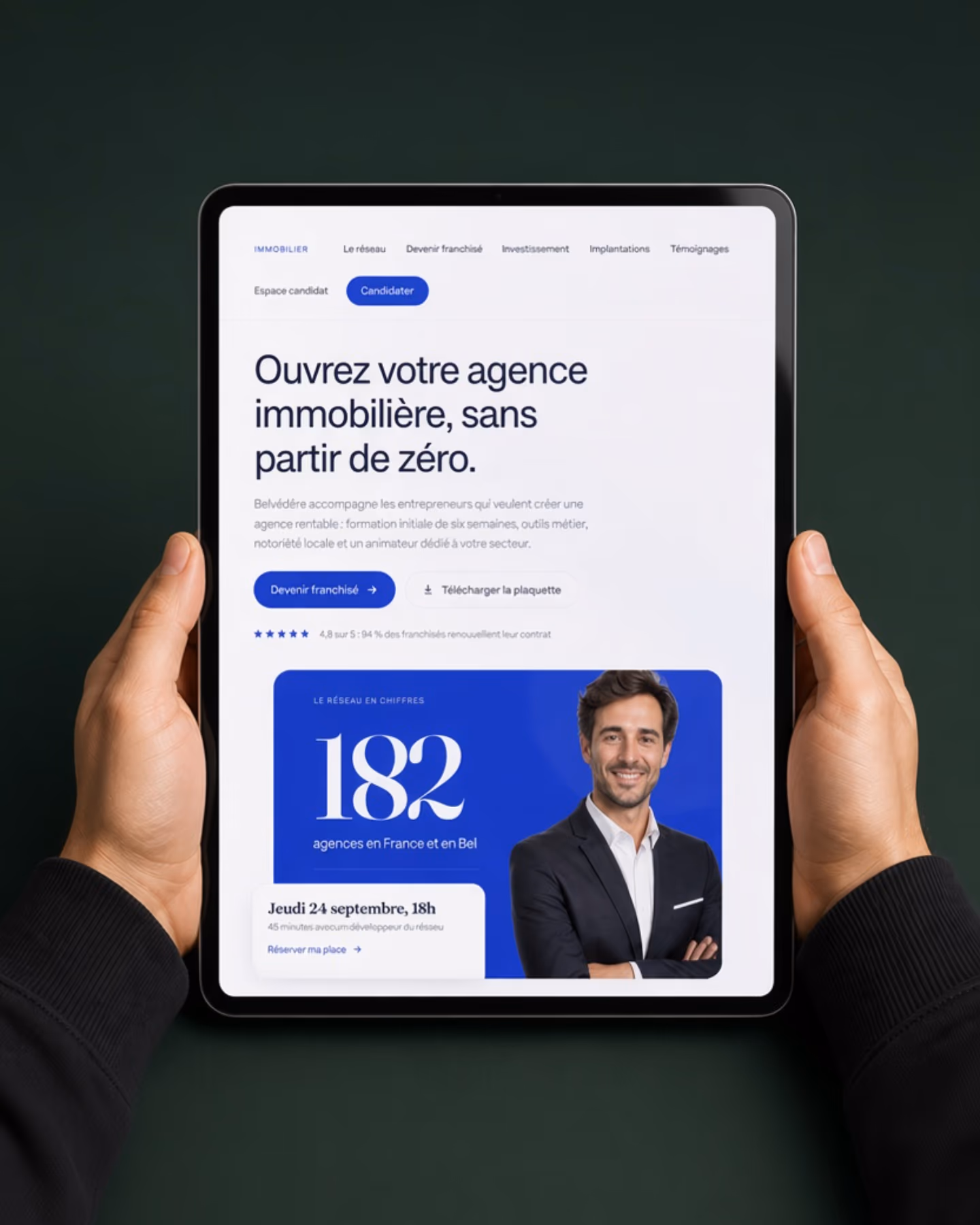 Le site web d'un réseau de franchise ouvert sur une tablette tenue à deux mains, navigation visible